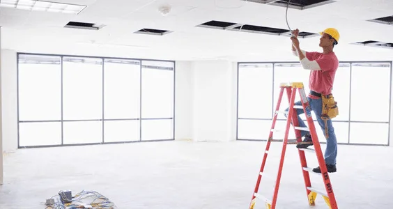 Electrician on a ladder installing ceiling wiring in an open commercial space