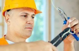 Electrician in a hard hat stripping a wire with pliers